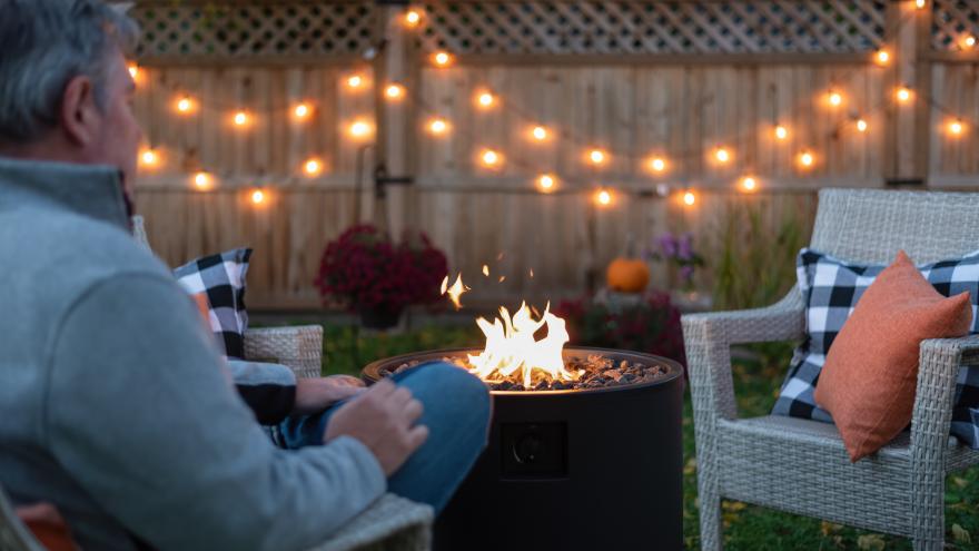 person on backyard patio with string lights and gas fire pit in the evening